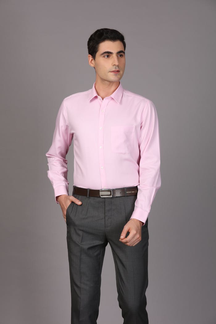 Professional man in pink shirt and gray pants posing confidently in studio setting.